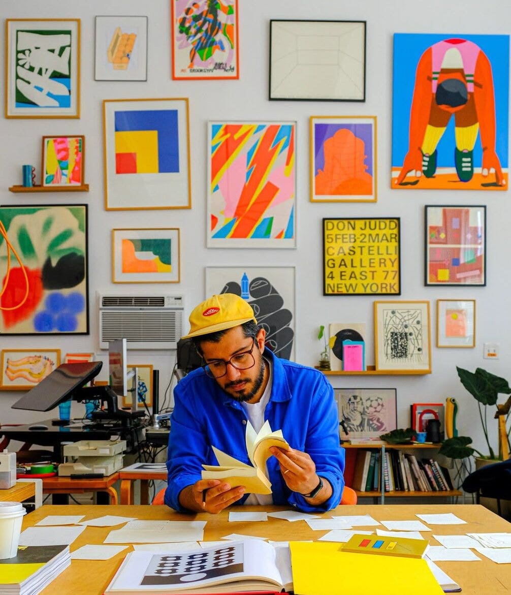A creator reads at a studio desk, with colorful art on the wall.