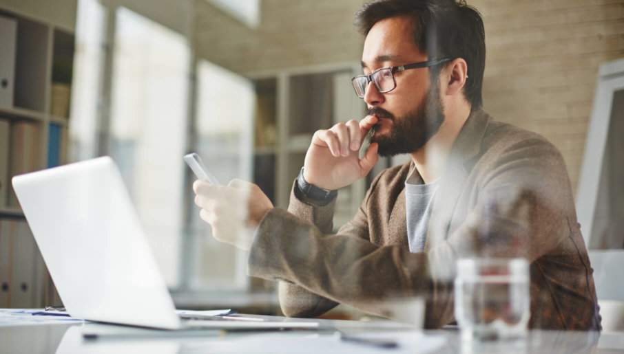 A man looking at his mobile device and laptop in order to decide what subscription business models to apply.