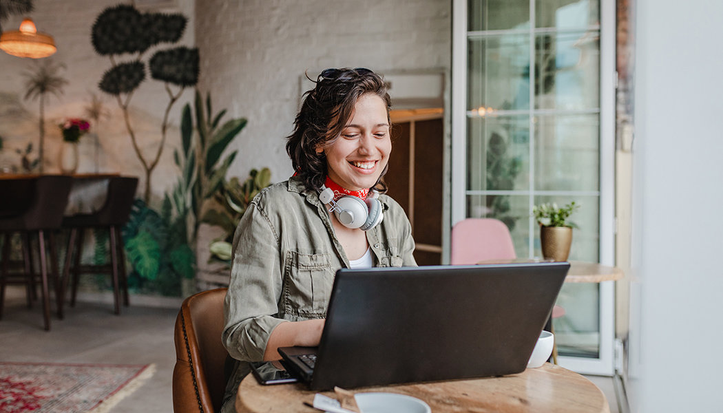 A woman smiles at her computer while researching Hotmart alternatives.