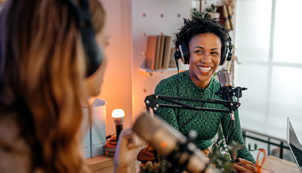 A Black woman smiles while recording a video podcast with her friend.