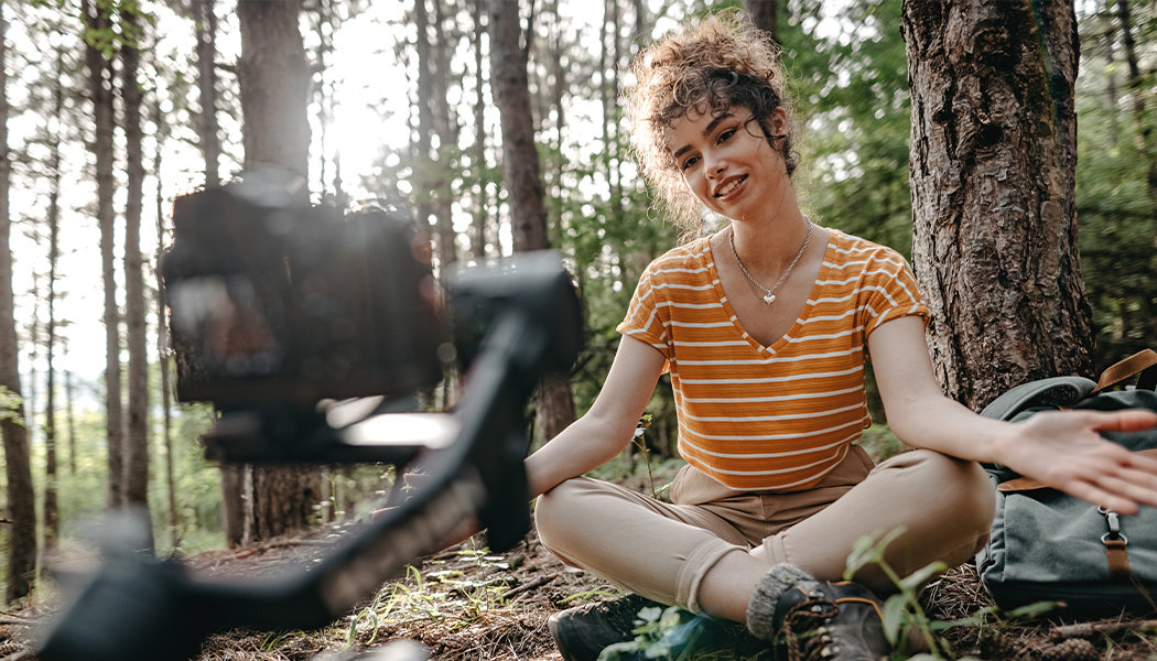 A woman sits in a forest while recording a video for YouTube