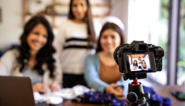 Three women stand in front of a camera live streaming for charity.