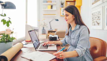 A woman takes notes while researching on her laptop how to create a membership site.