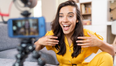 A woman talks to the camera while smiling indicating she's excited about talking to her members