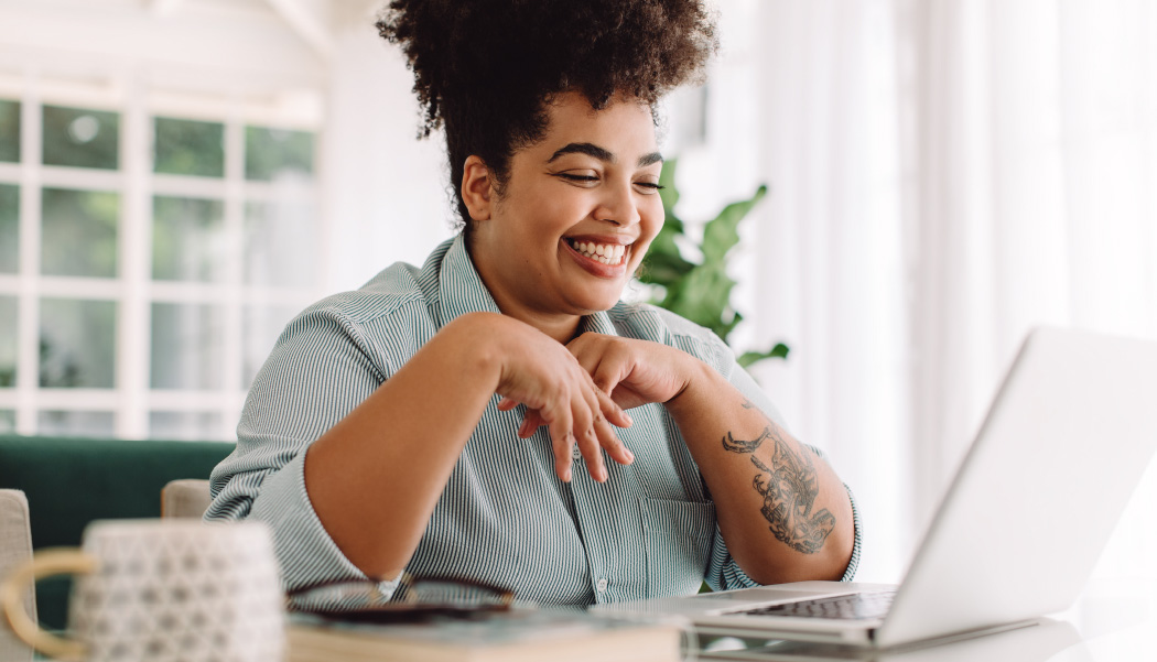 A woman smiles are her computer while looking for Patreon alternatives.