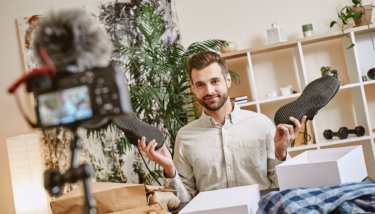 A man holds shoes in his hands while recording a video for his VOD platform.