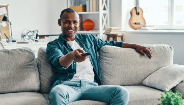 A man sits on his couch while using his Android TV app.