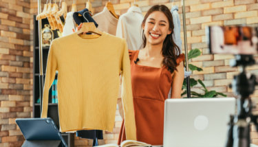 A woman shows off a yellow sweater during live stream a clothing haul.