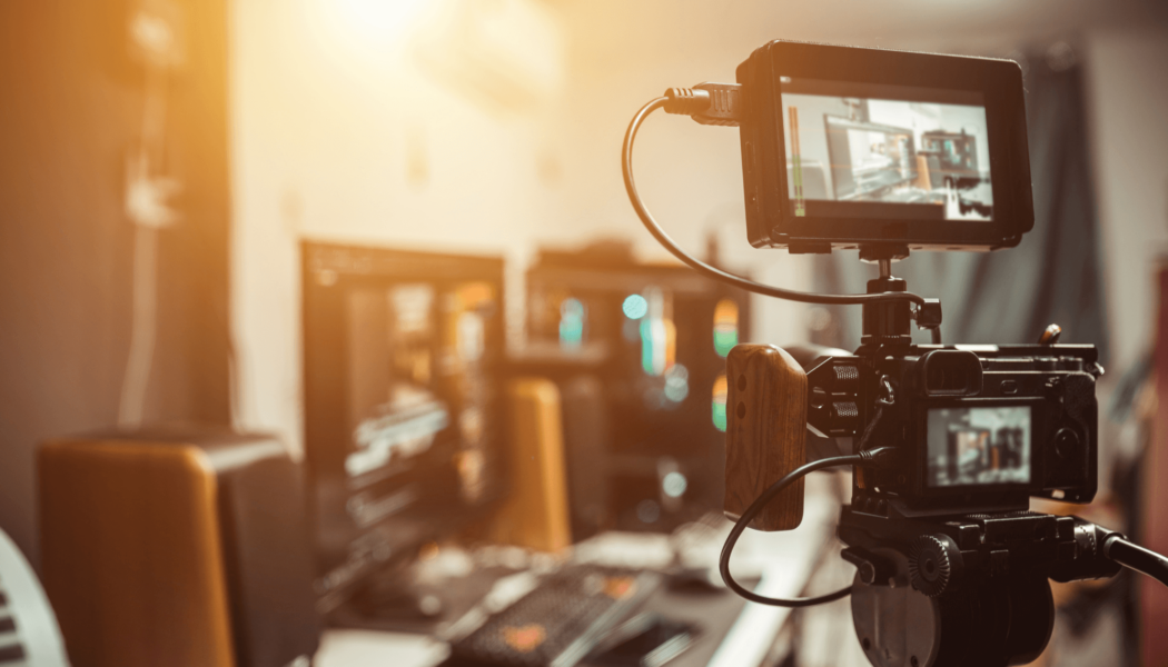 Photo of a desk and live streaming setup. This streaming setup includes a speaker, monitor, keyboard, mouse, computer tower. A camera is in the foreground of the photo.