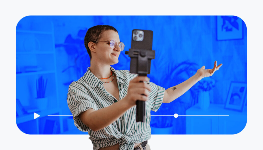 Creator talking to their phone on a mobile tripod with plants and a bookshelf behind them. Blue overlay with a video progress bar and play button.