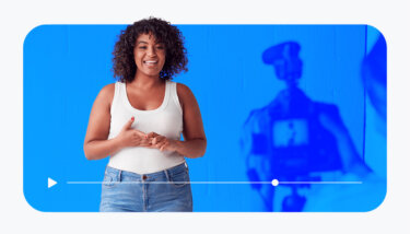 A woman smiling in front of a camera with a white brick background behind her.
