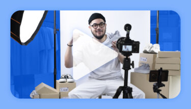 Man sitting in front of a camera holding up a shoe in front of a white backdrop and lights.